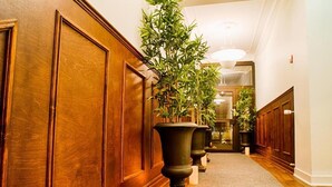 A hallway with wooden paneling, large black planters with green plants, and a carpeted floor. - H5 Hotel (Helsingborg)