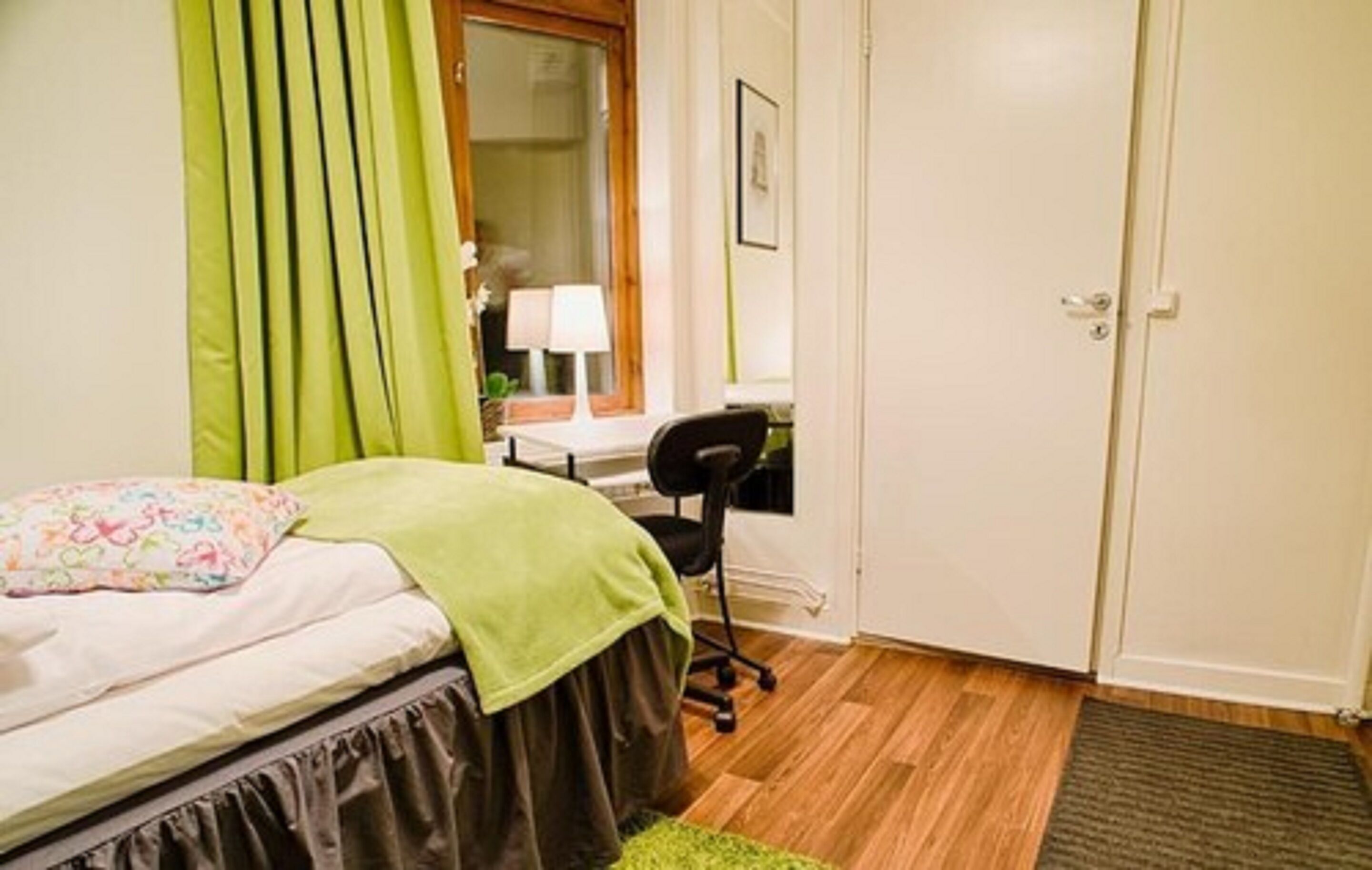 A bedroom with a bed, a desk, a chair, and a door.