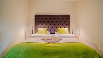 A neatly made bed with a green blanket and two pillows, a tufted headboard, and bedside lamps.