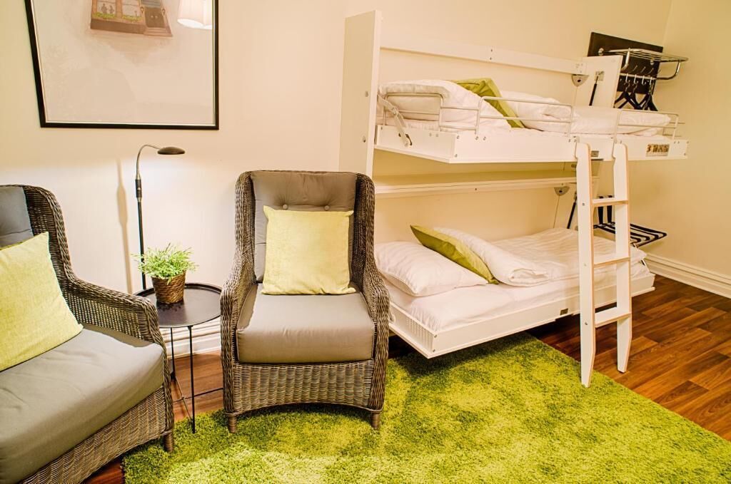 A room with a bunk bed, a wicker armchair, a small table with a plant, and a framed picture on the wall.
