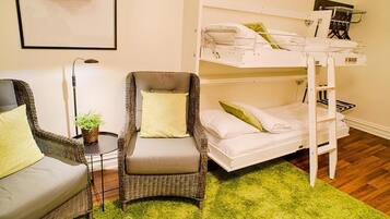 A room with a bunk bed, a wicker armchair, a small table with a plant, and a framed picture on the wall.