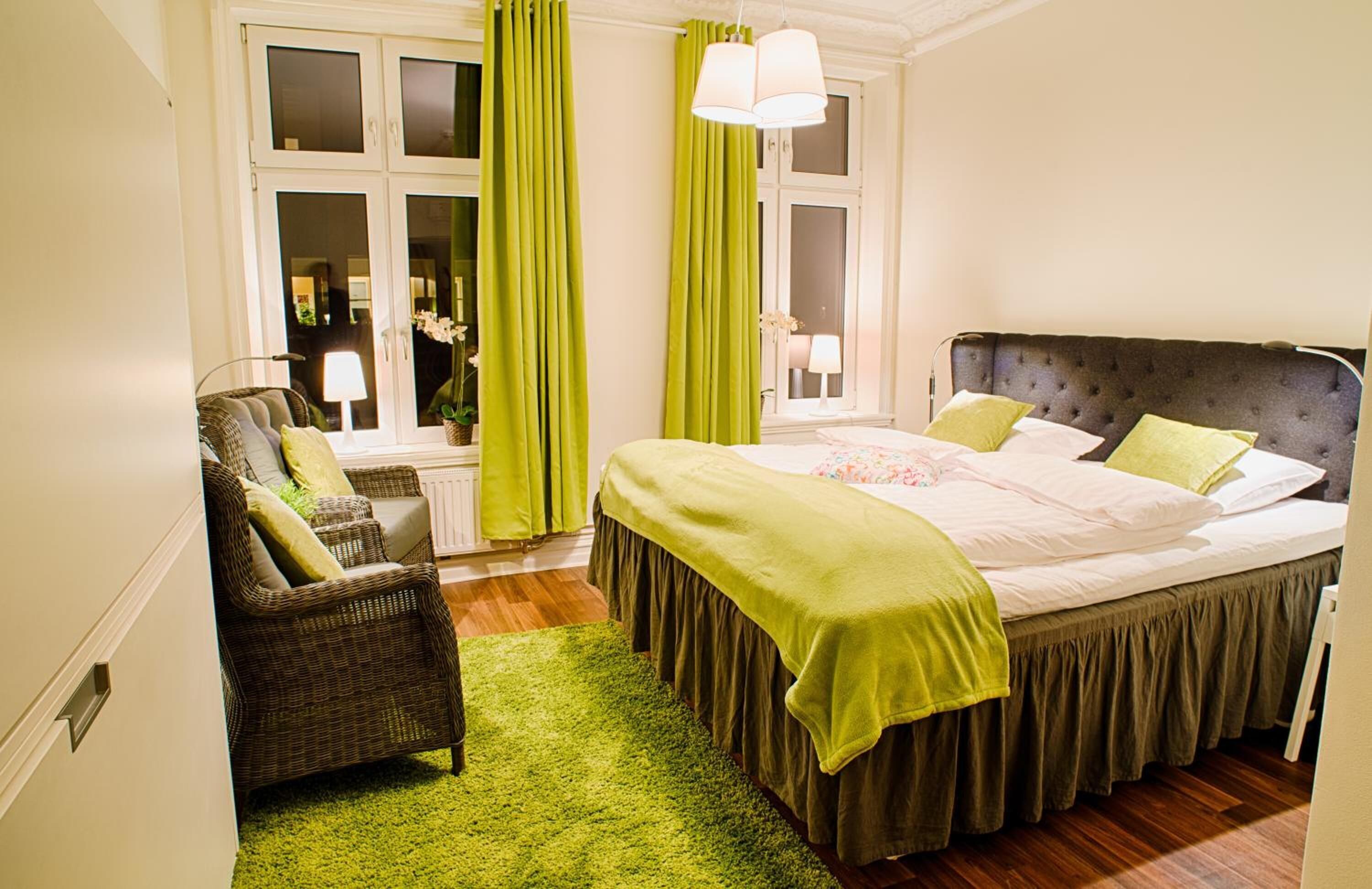 Ein Schlafzimmer mit einem großen Bett, einem Sessel, einem Fenster mit Vorhängen und einer Lampe.