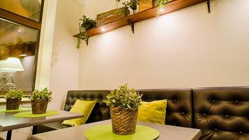 Interior acogedor de un restaurante con un sofá de cuero, manteles individuales verdes y plantas en macetas sobre las mesas.