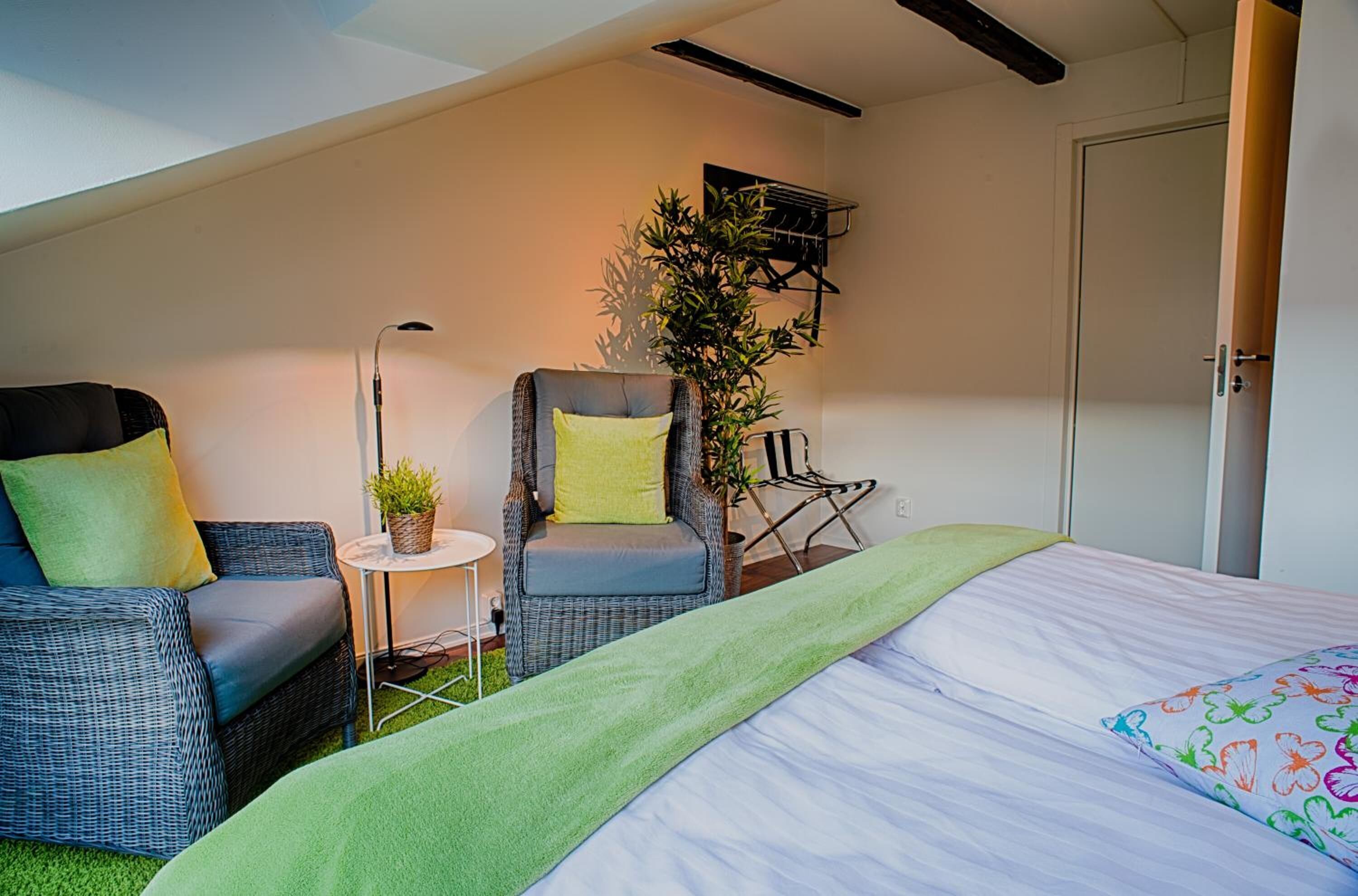 Un dormitorio con cama, una silla, una mesita con una planta y un estante en la pared.