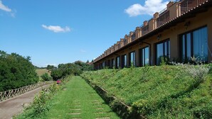 A pathway leading to a building with multiple windows and balconies, surrounded by greenery and a clear sky. - Francalancia Country Resort (Castelnuovo di Porto)
