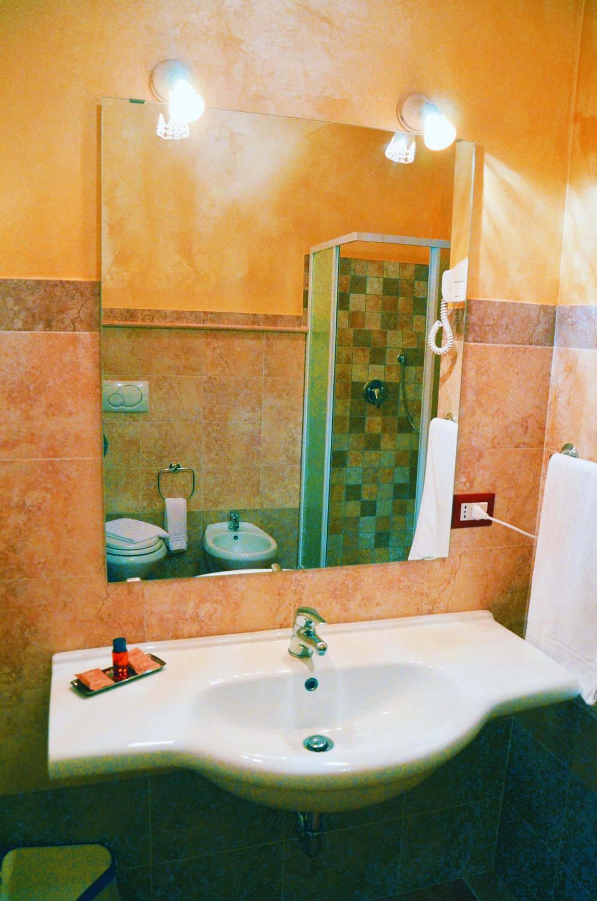 Un bagno con uno specchio grande, un lavandino, una doccia e un portascopevoli.