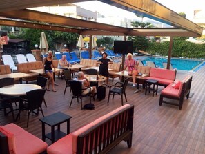 An outdoor seating area with tables and chairs, a pool in the background, and a covered section with umbrellas. - Sebnem Apart & Studios (Marmaris)