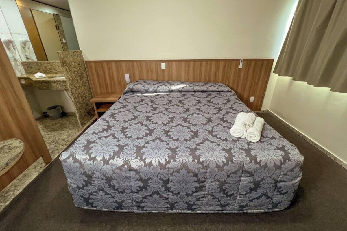 Een net opgemaakt bed met een bloemenprintdeken en twee opgerolde handdoeken erop.