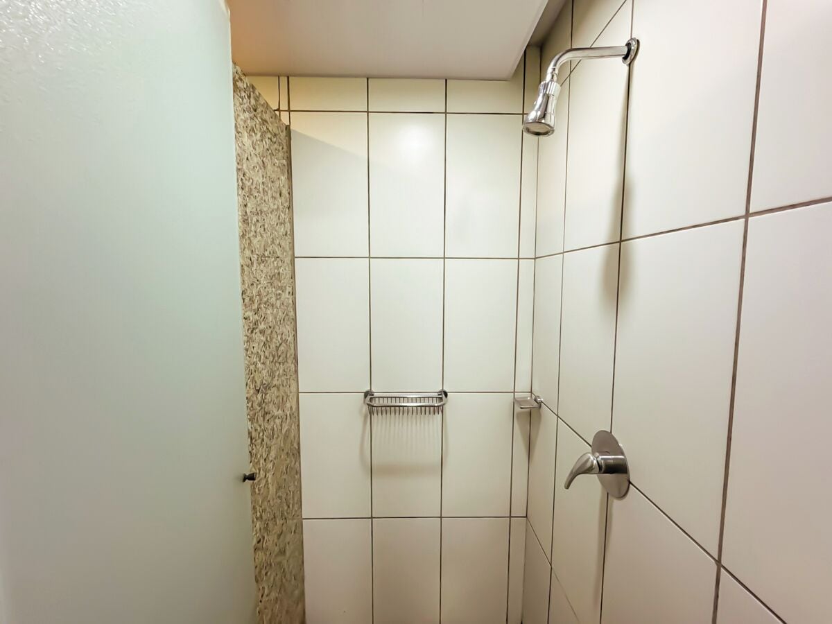 A bathroom with white tiled walls, a shower with a handheld showerhead, and a towel rack.