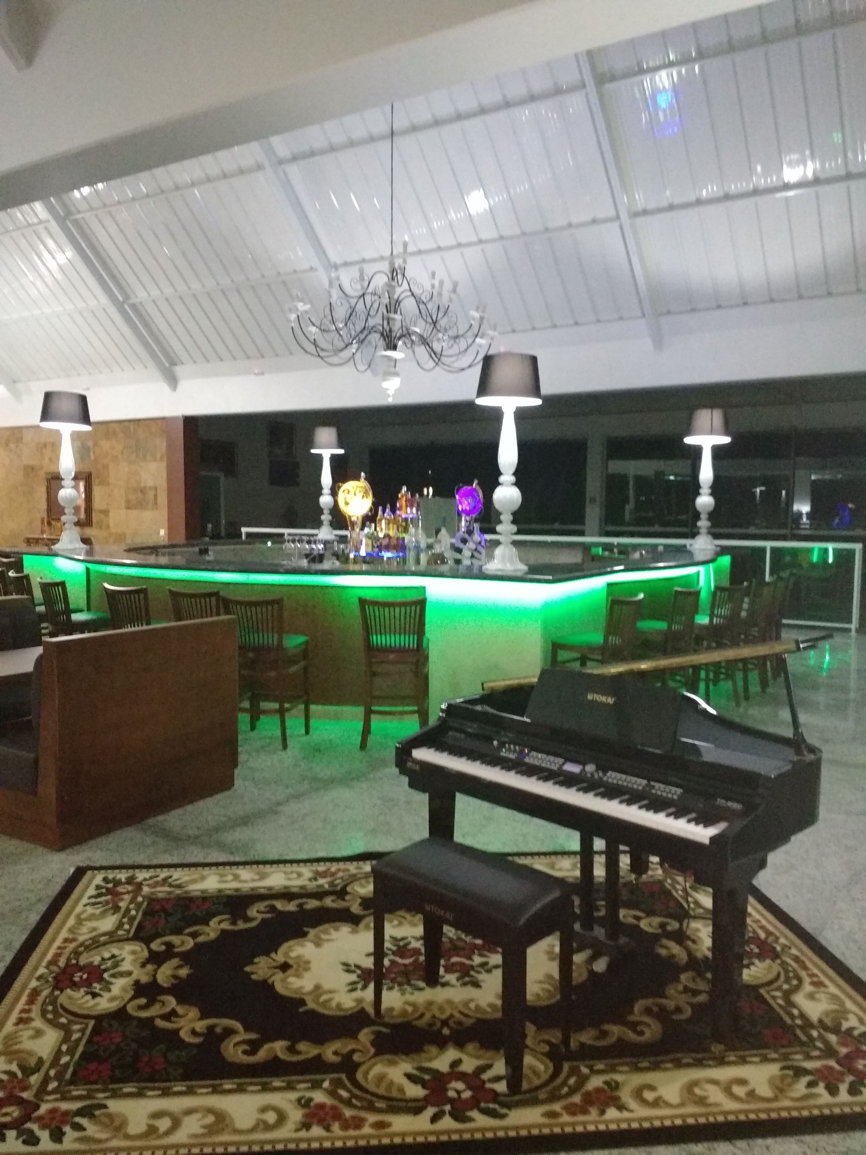 Eine geräumige Lobby mit einem Klavier, einer Bar mit grüner Beleuchtung und einem Kronleuchter.