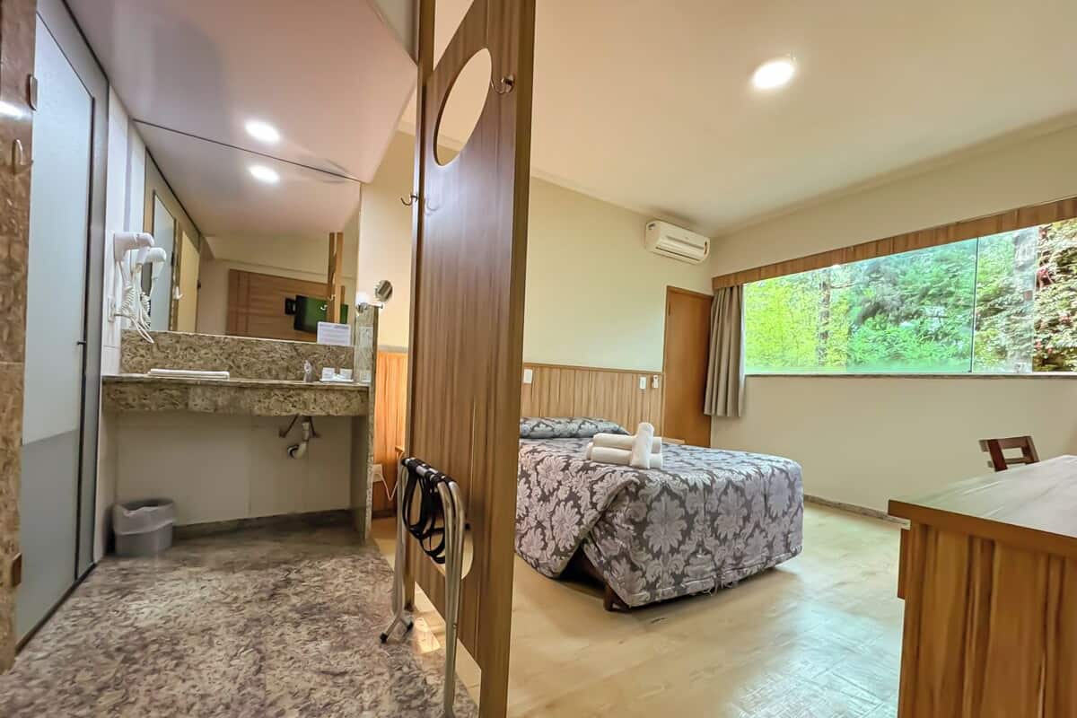 Een hotelkamer met een bed, een bureau, een badkamer en een groot raam met uitzicht op groen.