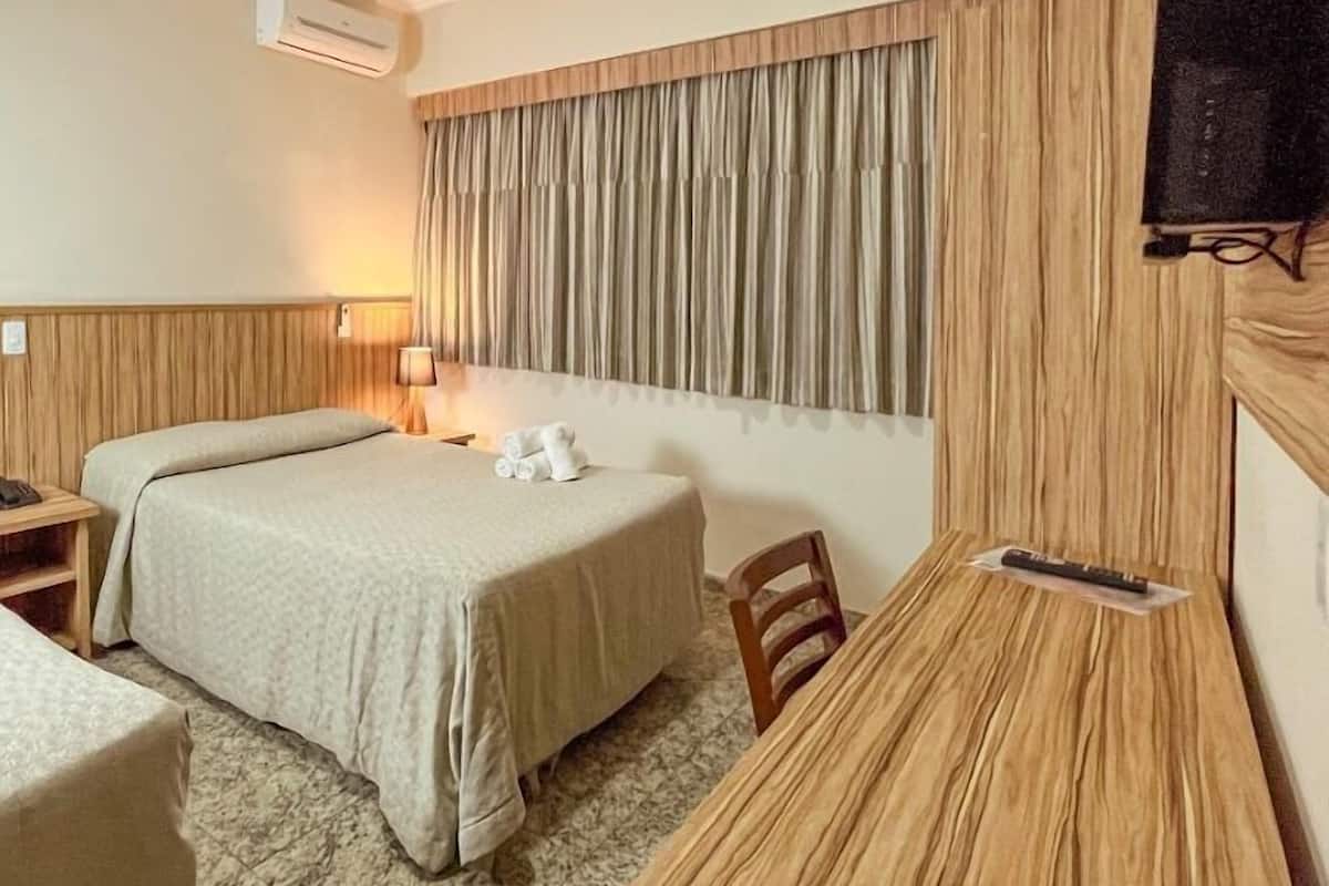 Een hotelkamer met een bed, een bureau, een stoel, een lamp en een airconditioning.