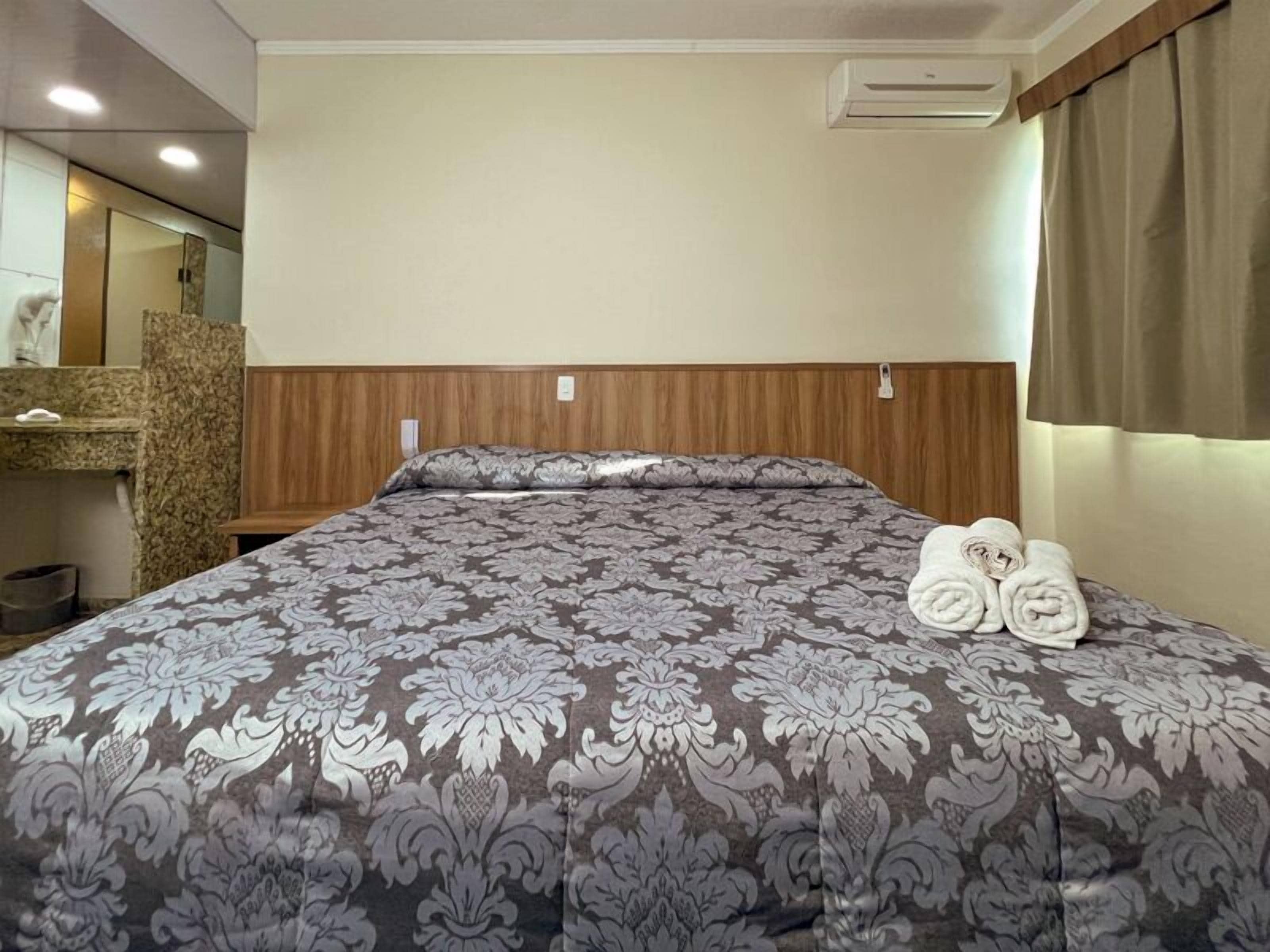Una habitación de hotel con cama, cabecera de madera, baño con espejo y una toalla sobre la cama.