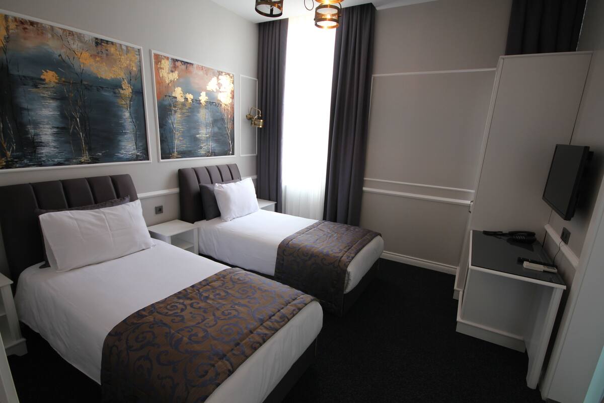 A hotel room with two beds, a TV, and artwork on the wall.