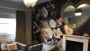 A room with a fireplace, two tufted armchairs, a floral mural, and a large mirror. - Town House at Brecon (Brecon)