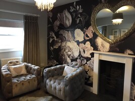 Una habitación con chimenea, dos sillones tapizados, un mural floral y un espejo grande.