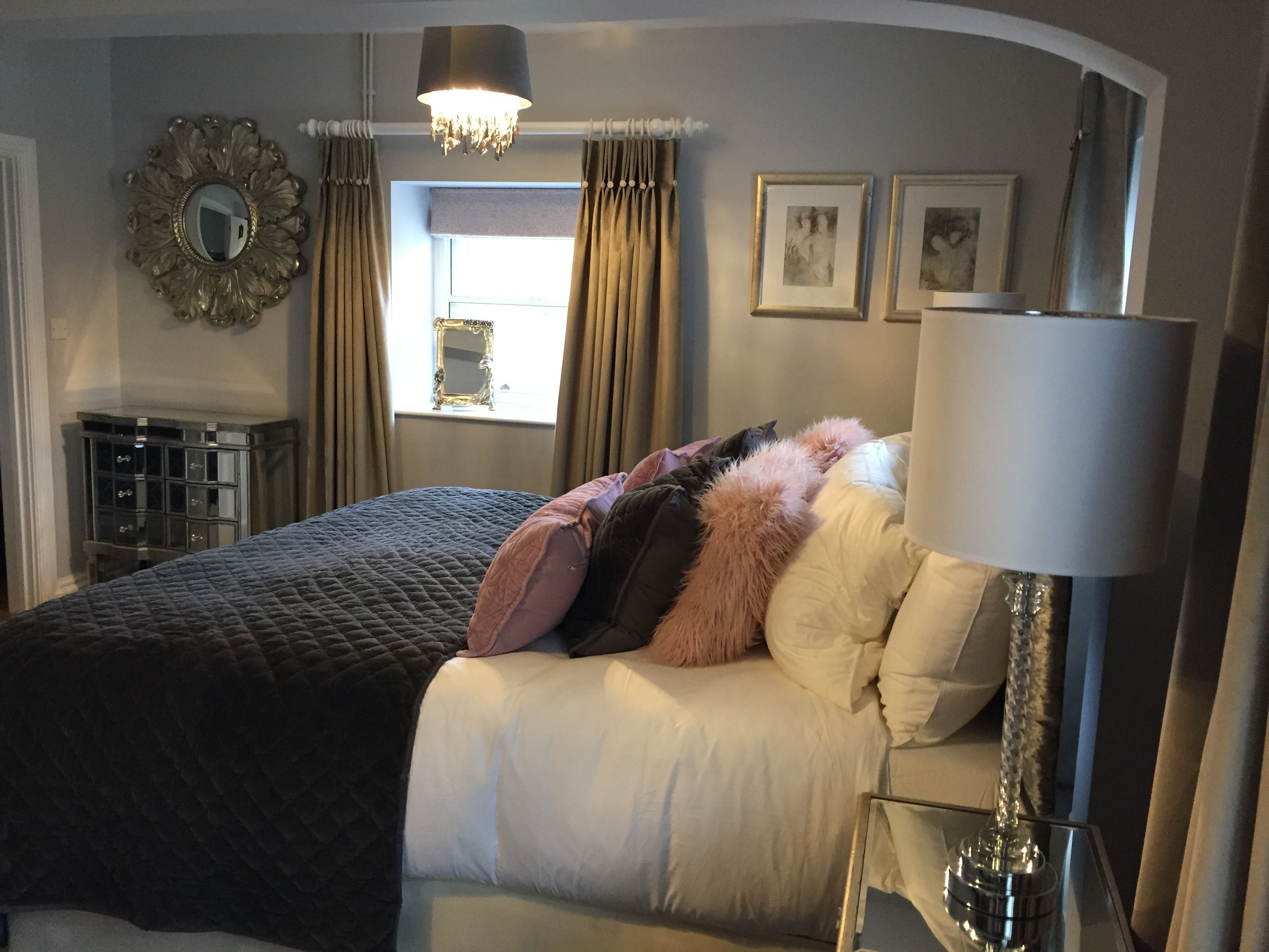 A bedroom with a bed, a mirror, a chandelier, curtains, and framed pictures on the wall.