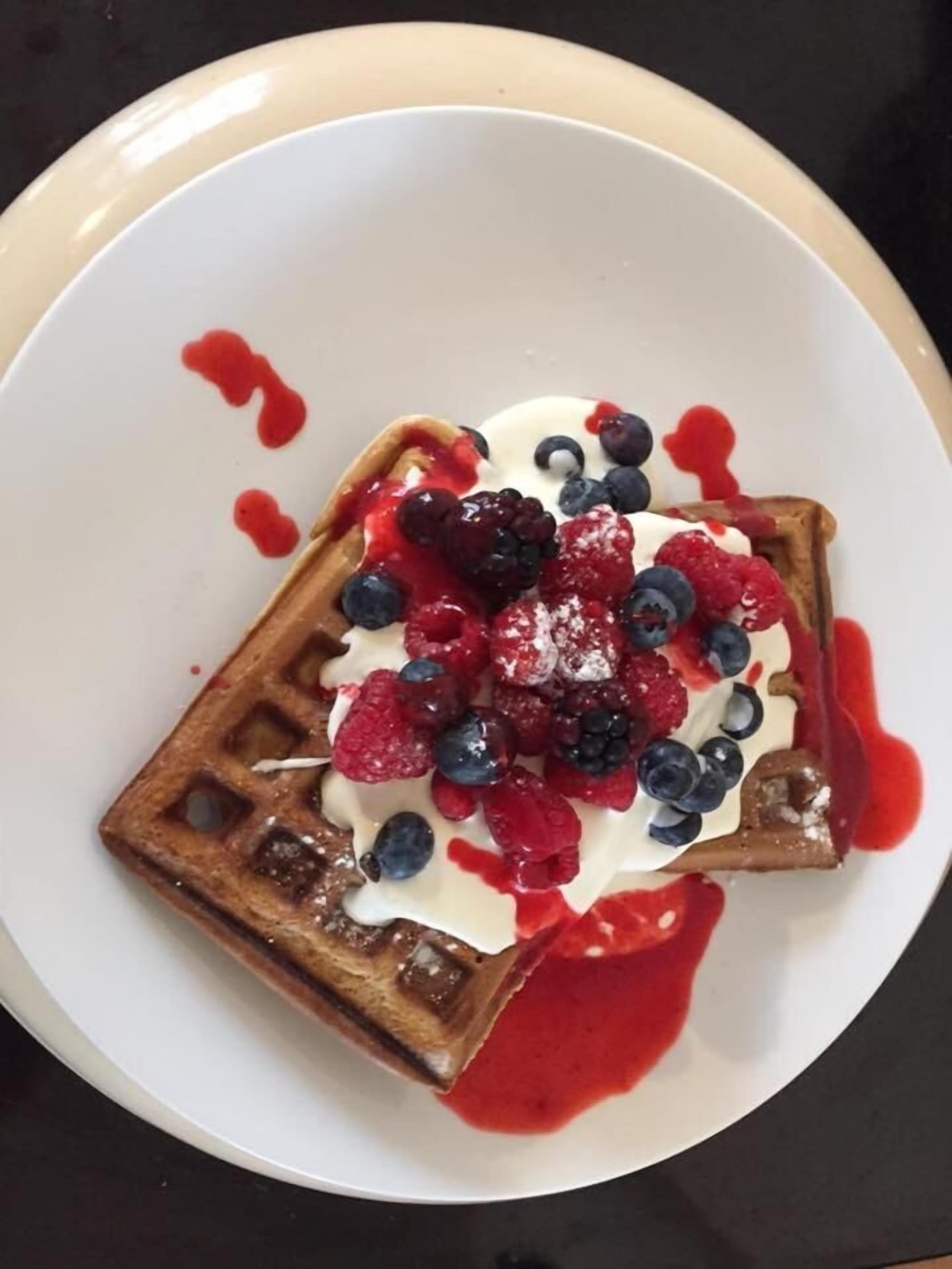 Gofre cubierto de frutos rojos y crema batida sobre un plato blanco.