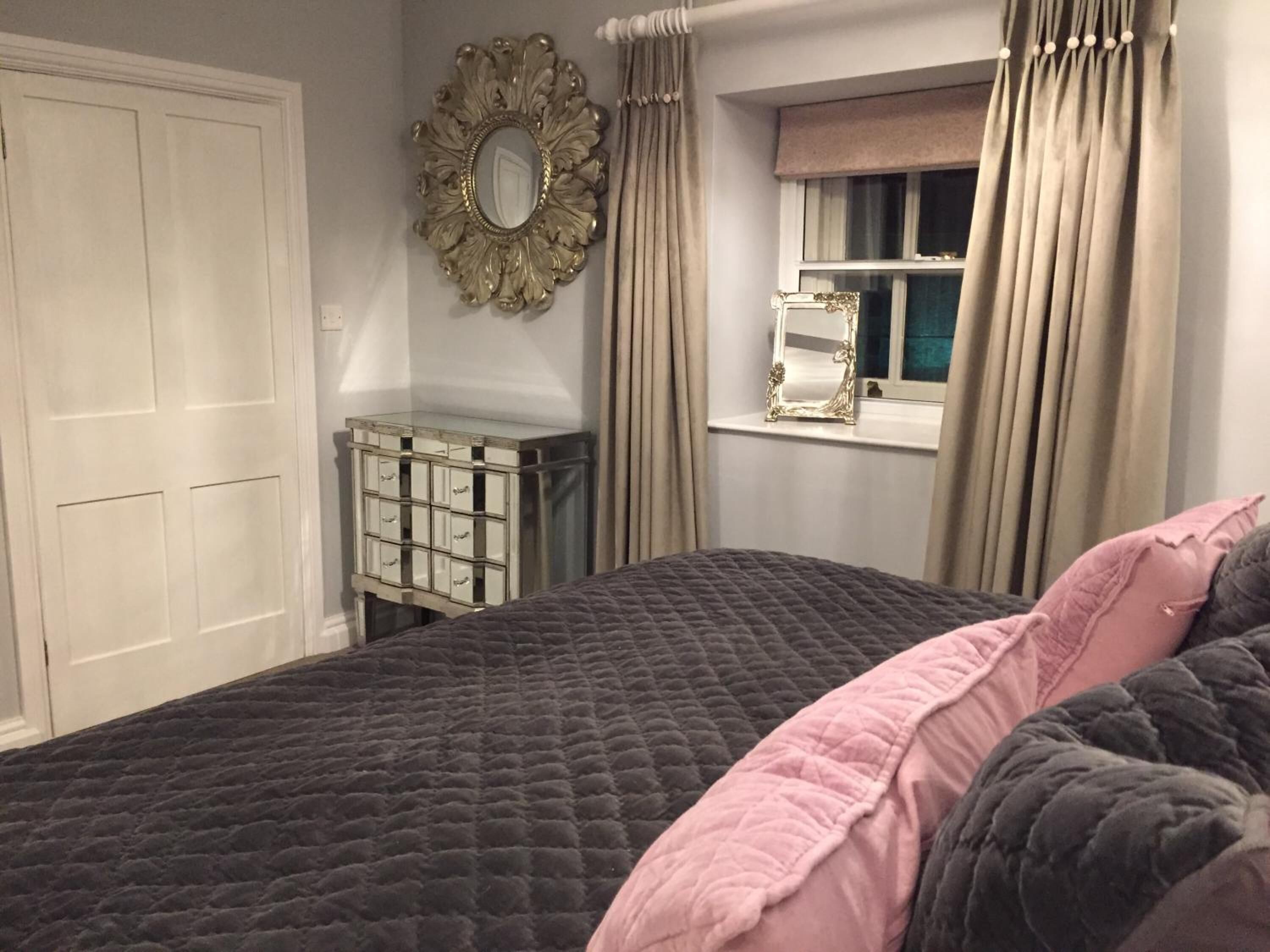 Un dormitorio con una cama grande, un aparador con cajones, un espejo y una ventana con cortinas.