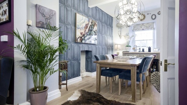 A dining area with a wooden table and blue upholstered chairs, a potted plant, and a decorative rug. - Town House at Brecon (Brecon)