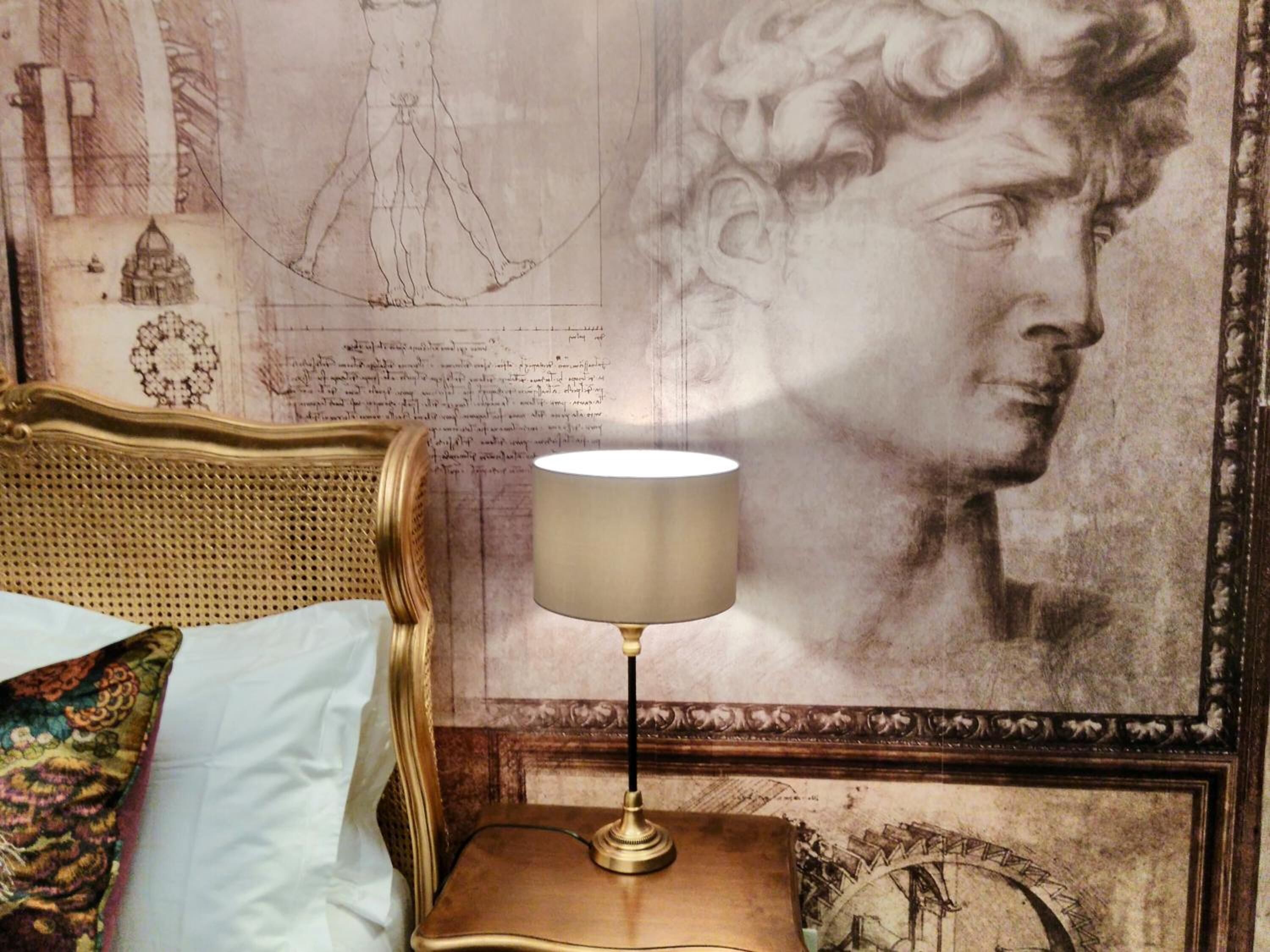 Una habitación con una cama, una lámpara en una mesita de noche y una obra de arte grande en la pared.