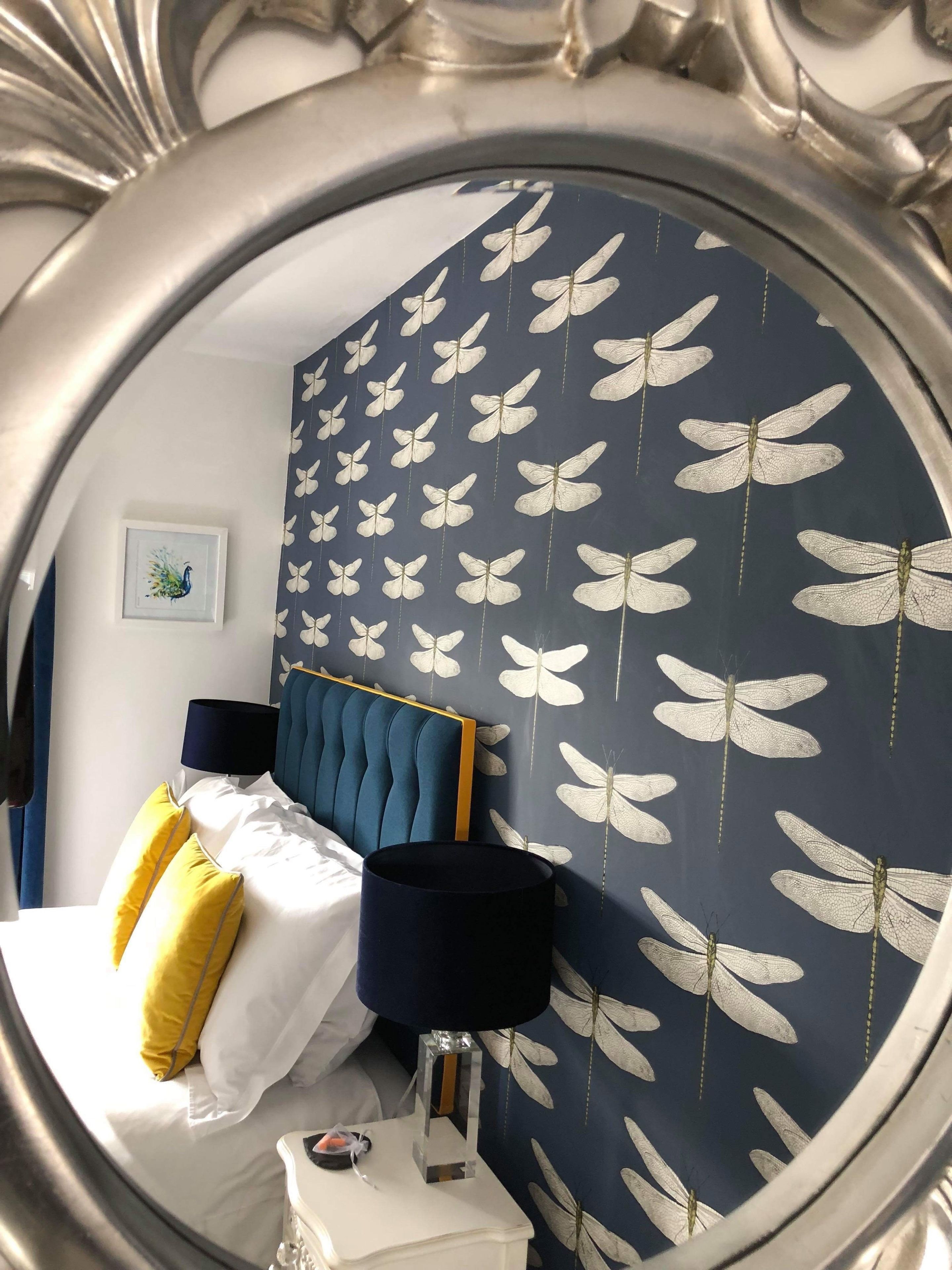 A bedroom with a bed, a nightstand, a lamp, and a wall with a butterfly pattern.