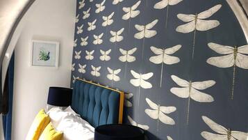 A bedroom with a bed, a nightstand, a lamp, and a wall with a butterfly pattern.