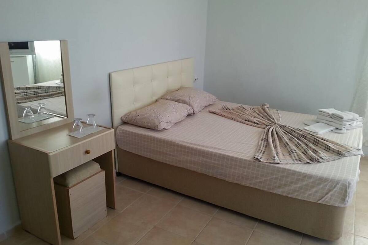 A bedroom with a bed, a bedside table with a mirror, and a small drawer unit.