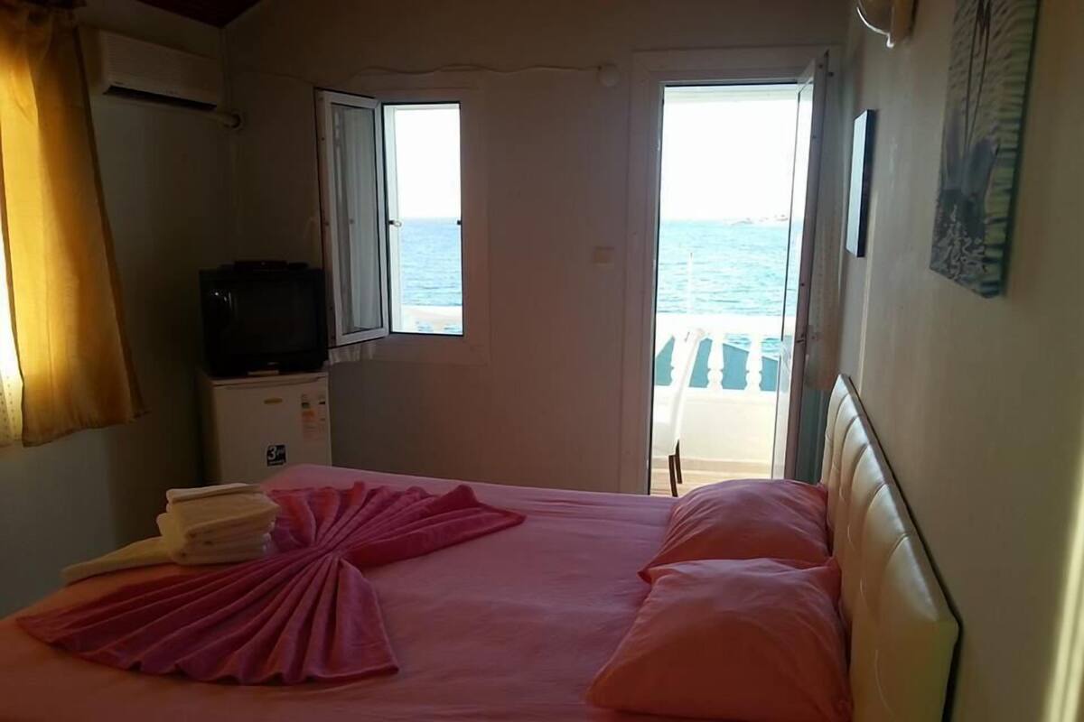A room with a bed, a television, and a view of the sea through an open door.