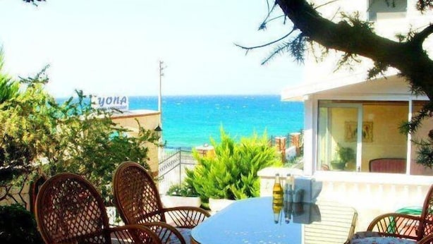 Un patio con mobiliario de mimbre y una mesa, con vista a un mar azul y despejado.