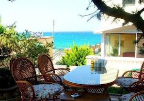 Un patio con mobiliario de mimbre y una mesa, con vista a un mar azul y despejado.