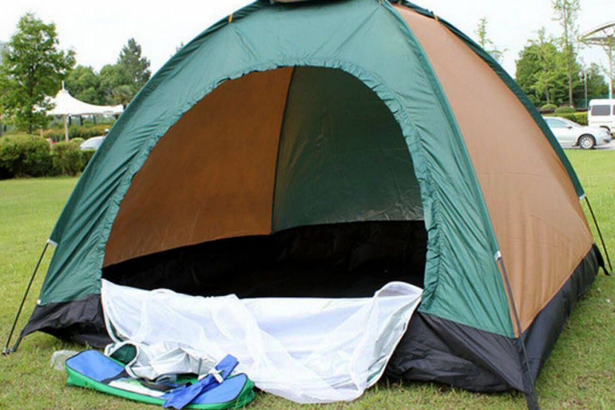 A dome-shaped tent with a green and brown color scheme, set up on grass with a white rain cover and camping gear nearby.