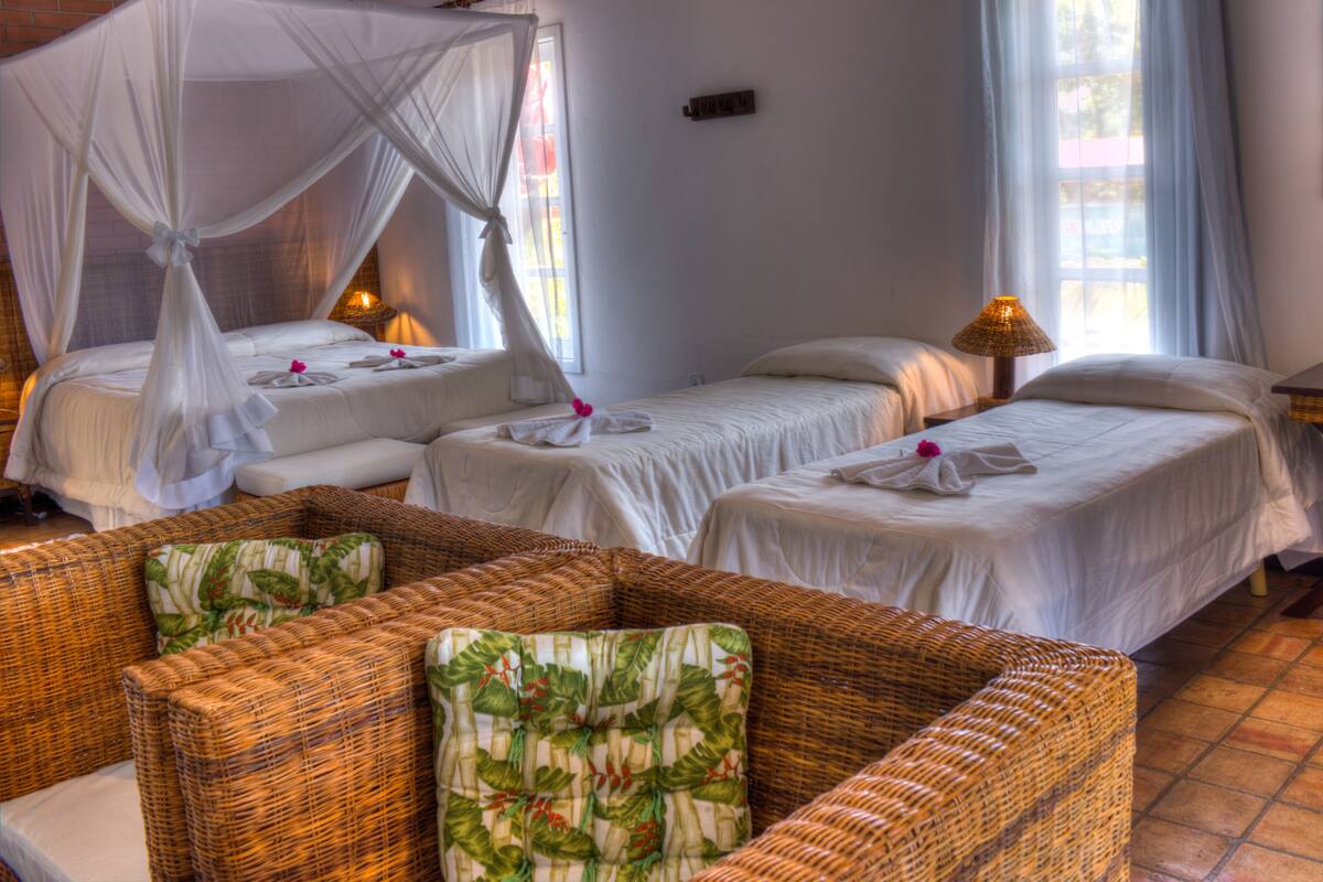 A hotel room with two single beds, a wicker sofa, and a canopy bed.