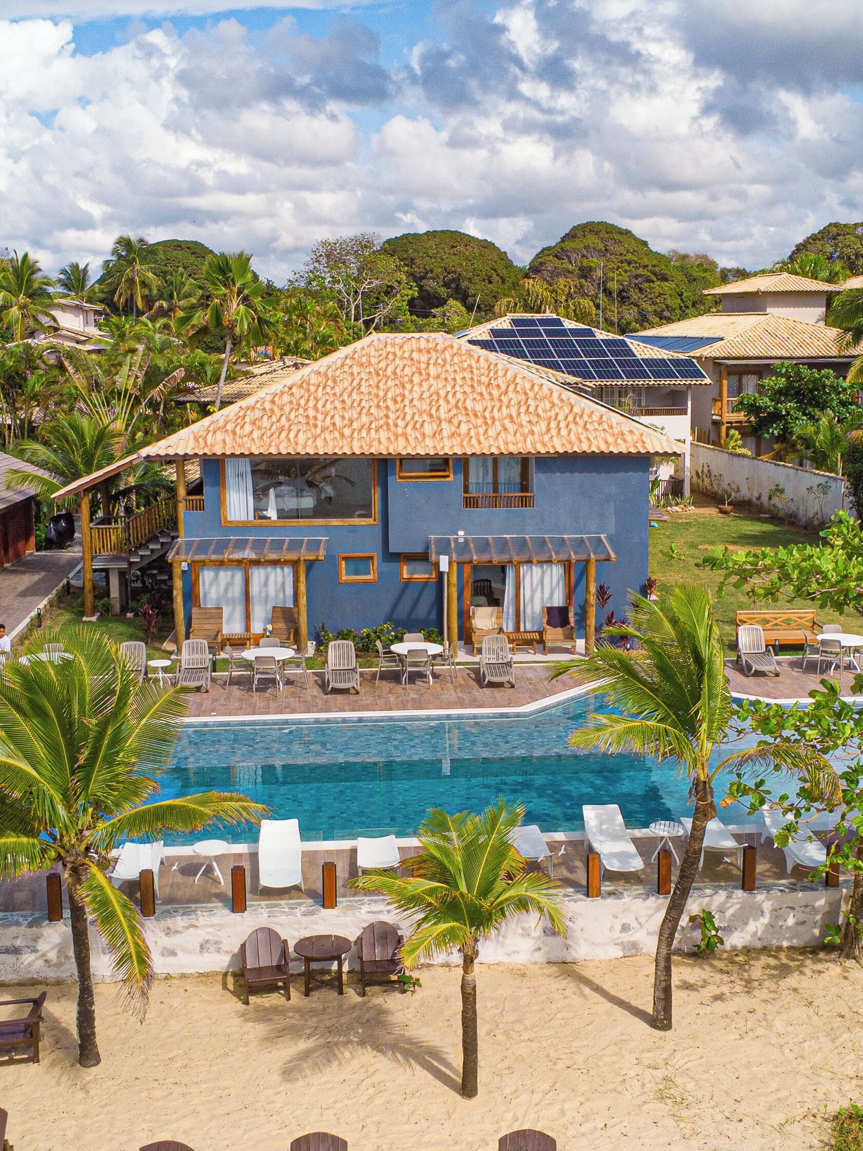 A two-story building with a swimming pool, surrounded by palm trees and lounge chairs.