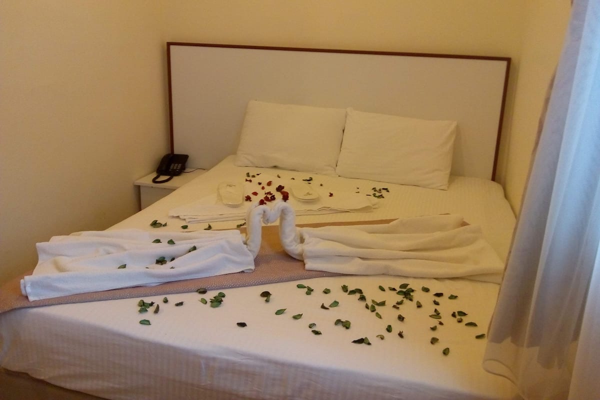 A hotel room with a neatly made bed, a bedside phone, and a small table with a glass and a plate.