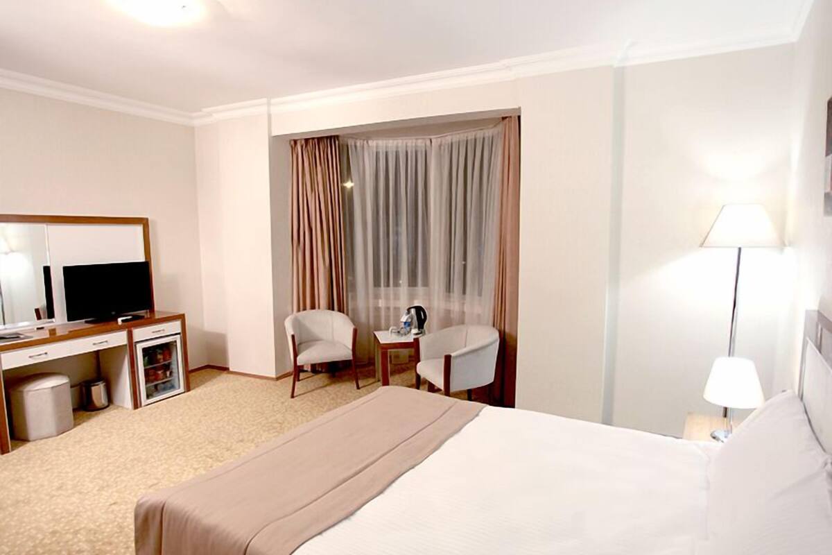 Habitación de hotel con cama, escritorio con televisor, una silla, una mesita y una lámpara.