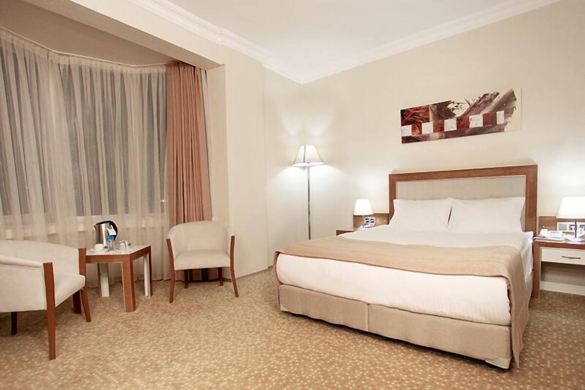 Una habitación de hotel con una cama grande, una silla, una mesita, una lámpara y un cuadro en la pared.