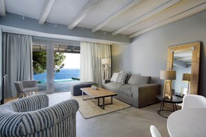 Un salon moderne avec un canapé, un fauteuil et une table basse, de grandes fenêtres avec des rideaux et une vue sur la mer.