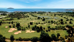 Un parcours de golf avec des bunkers, des arbres et une vue sur la mer.