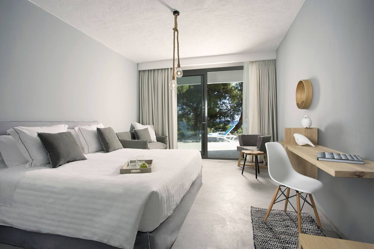 Een moderne hotelkamer met een groot bed, een bureau met stoel, een laptop en uitzicht op het omliggende landschap.