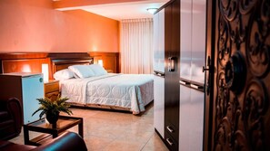 A hotel room with a bed, bedside table, lamp, and a potted plant.