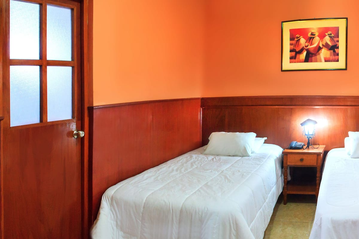 A hotel room with two single beds, a wooden nightstand with a lamp, and a painting on the wall.