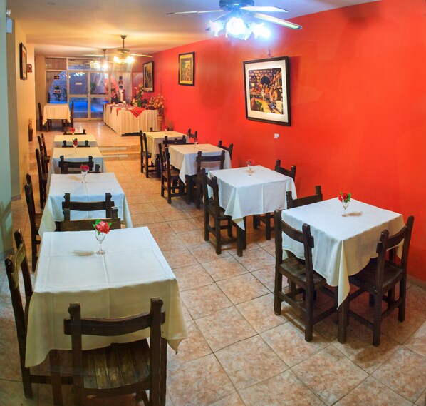 Un restaurante con varias mesas y sillas, una pared roja y un ventilador de techo.