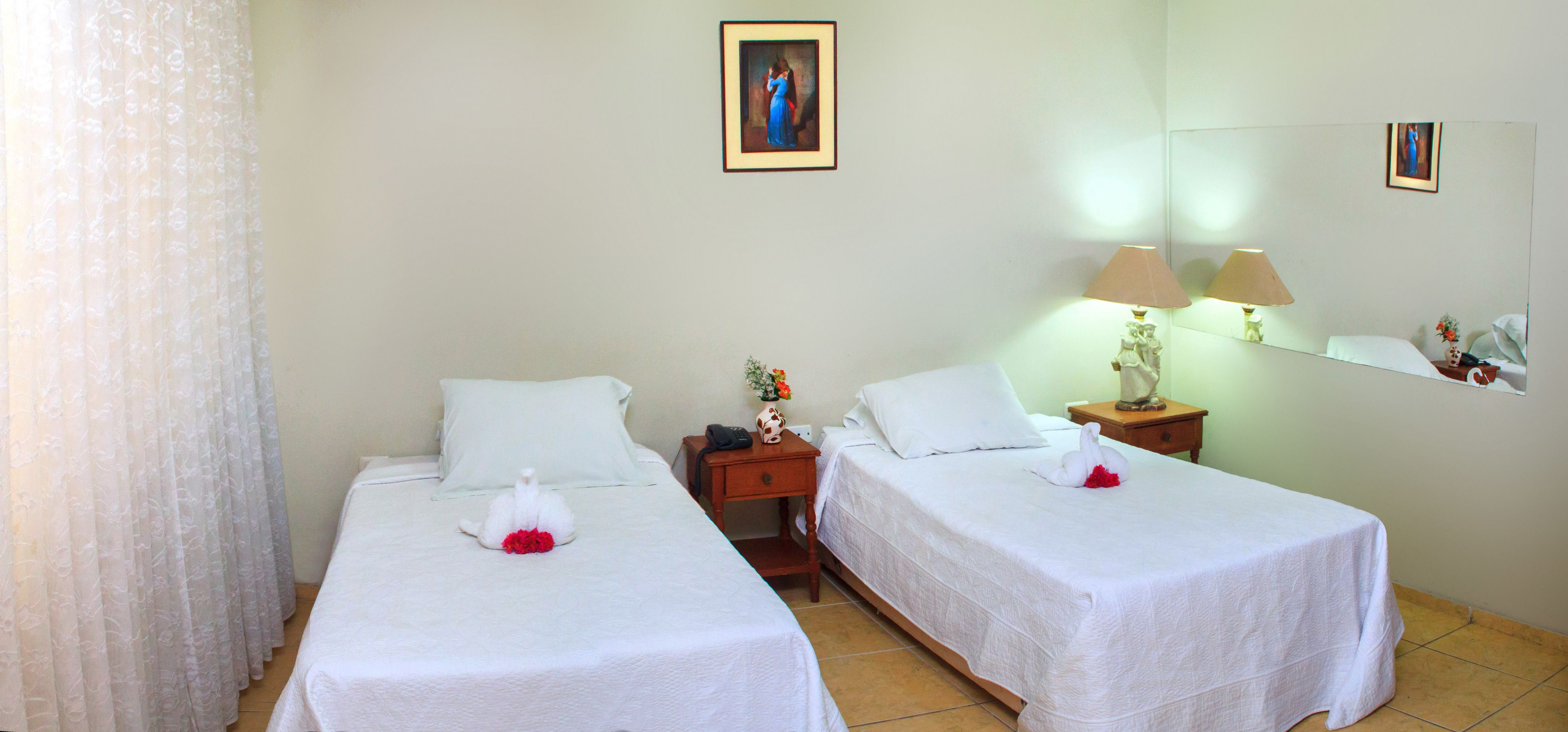 Una habitación de hotel con dos camas individuales, una mesita de noche con una lámpara y un espejo en la pared.
