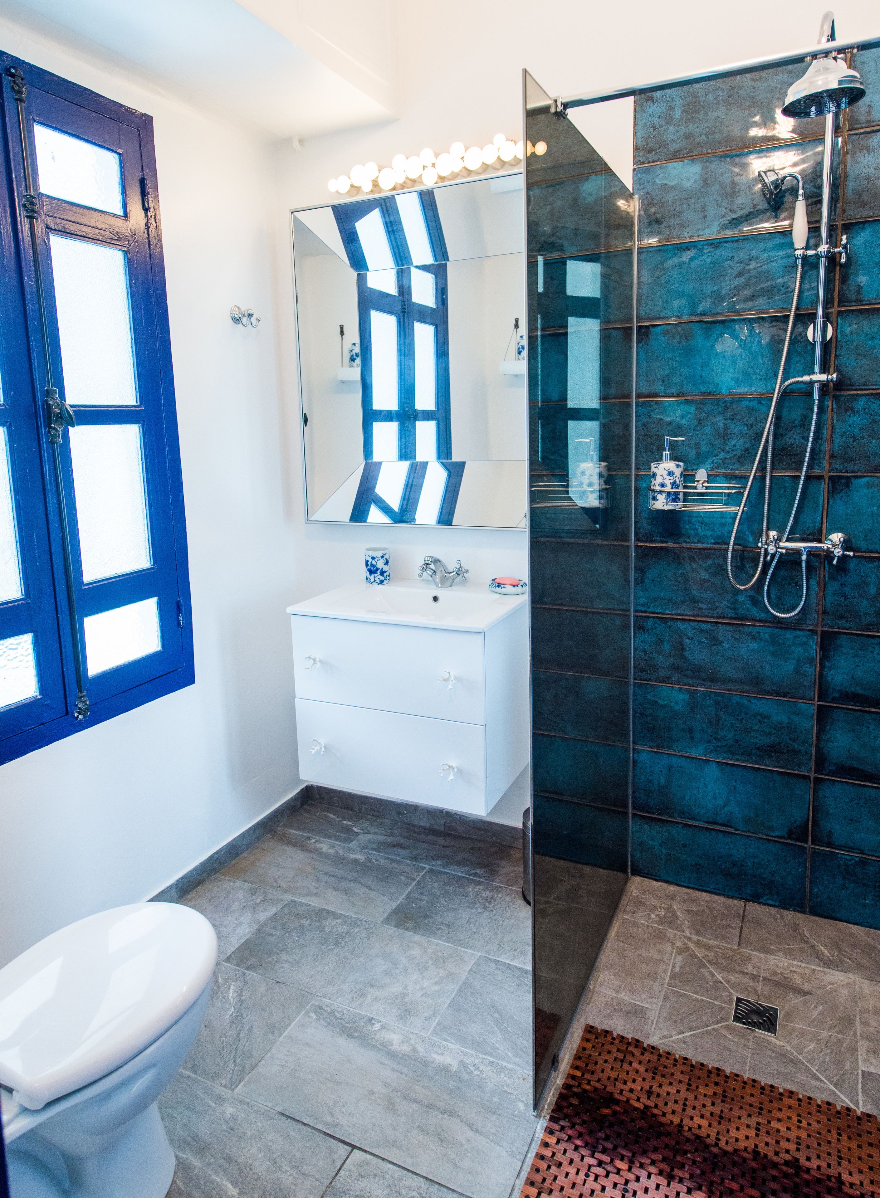 Un baño con lavamanos blanco, espejo, ducha y ventana con marco azul.