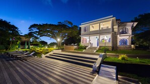 A two-story house with a wooden deck, outdoor seating, and a well-lit garden. - Apolline Martinique (Fort-de-France)