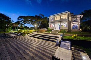 Une maison à deux étages dotée d’une terrasse en bois, d’un espace salon extérieur et d’un jardin bien éclairé.