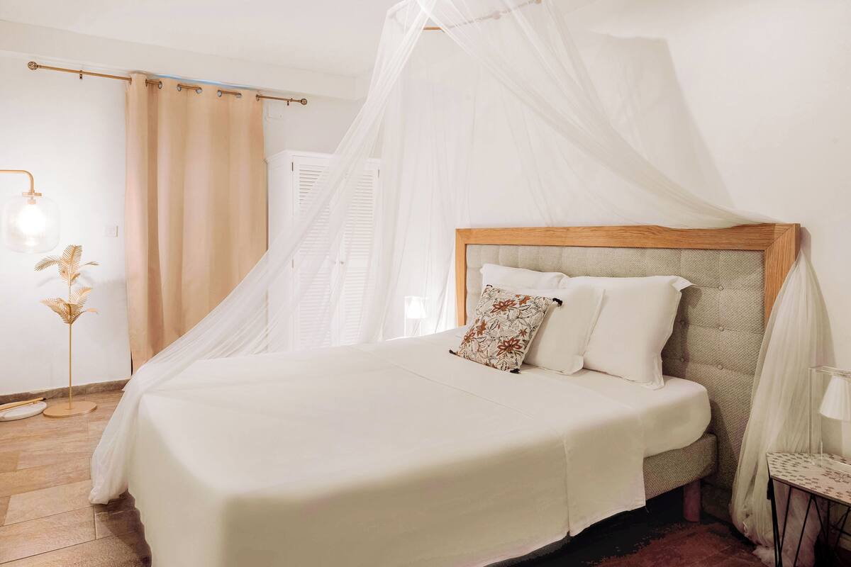 A neatly made bed with a canopy, a bedside table with a lamp, and a floor lamp.