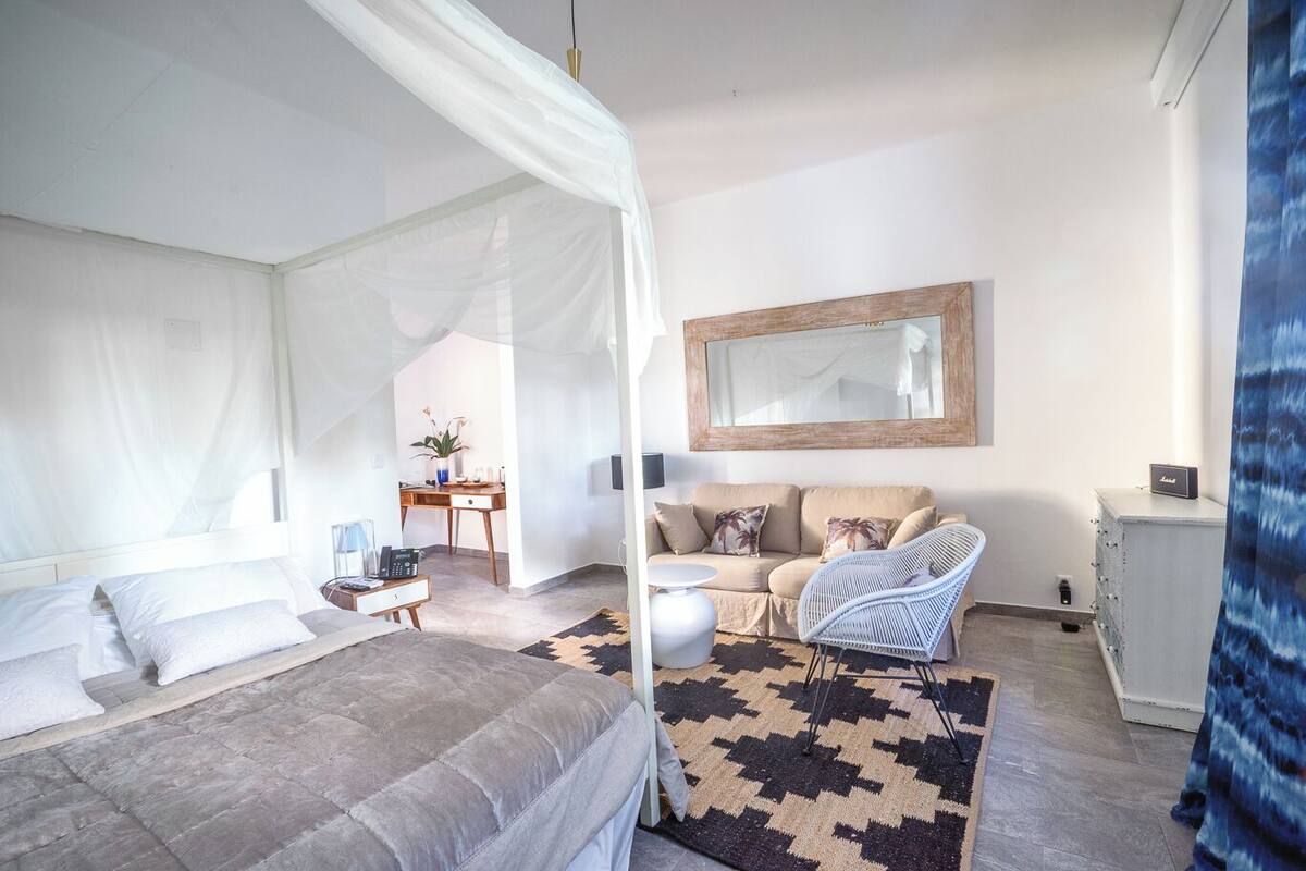 A bedroom with a canopy bed, a sofa, a desk, and a mirror.