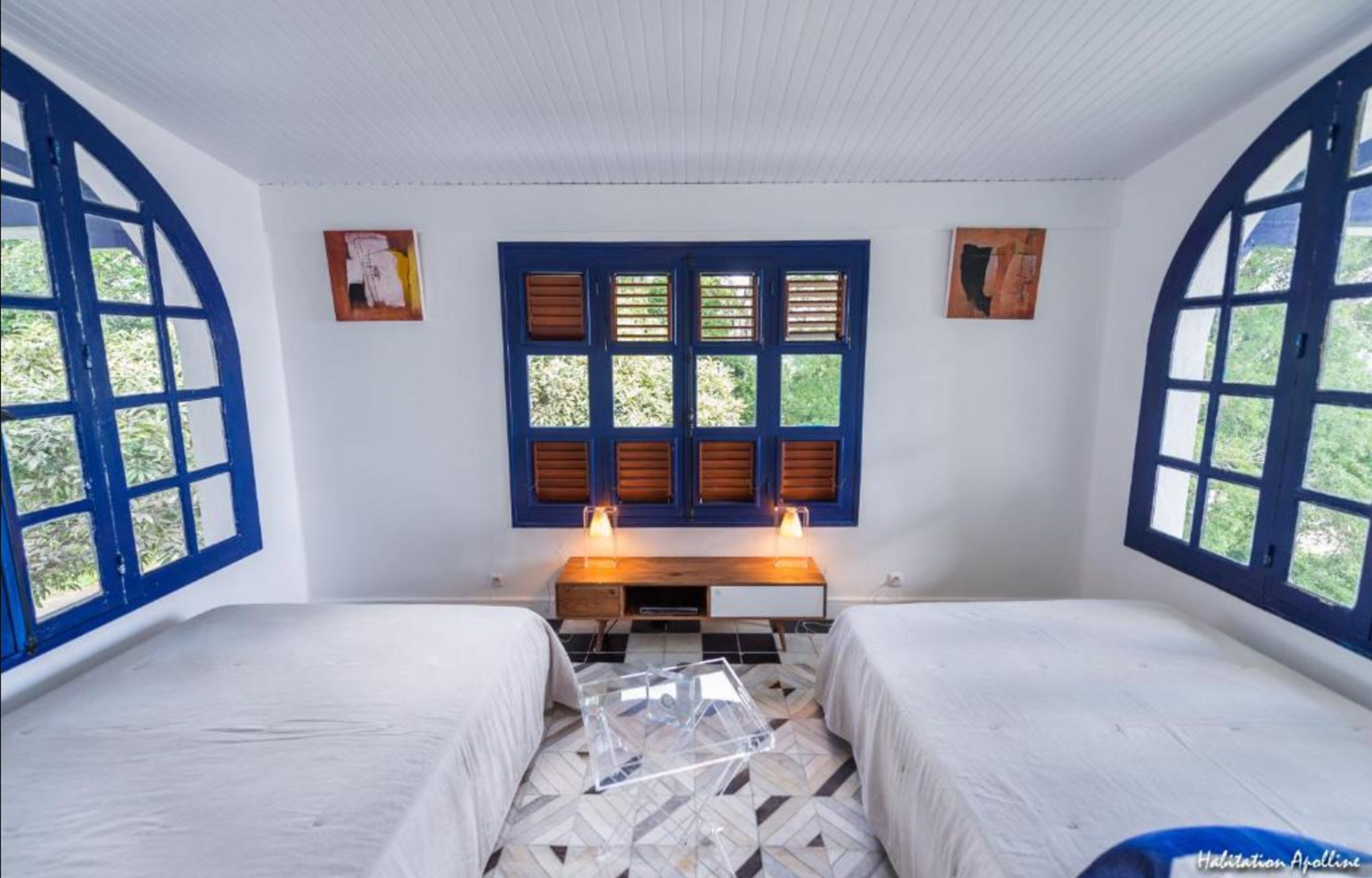 Une chambre avec deux lits, une table de chevet en bois et une fenêtre avec des volets.